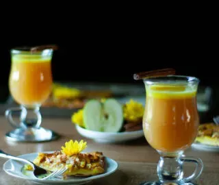 dos vasos de ron con mantequilla caliente chai de cúrcuma con una rodaja de tarta de manzana.' title=