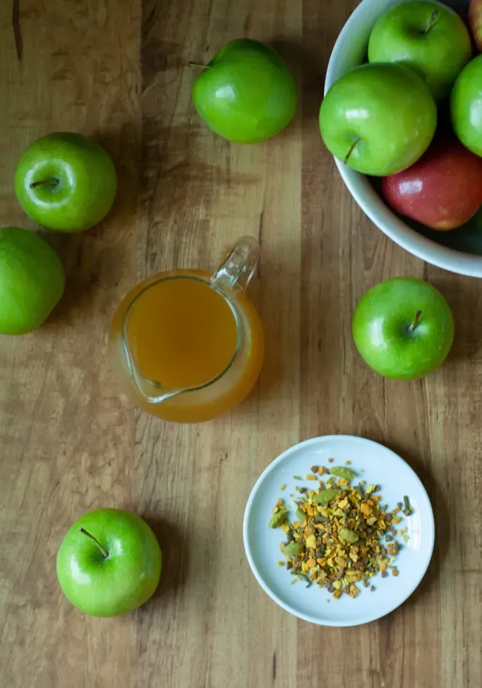 manzanas verdes sobre una mesa de madera con una jarra de almíbar dorado y té de hojas sueltas.' loading='lazy' title=