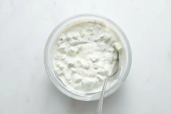Uma tigela de tzatziki de pepino e endro sendo mexida com uma colher