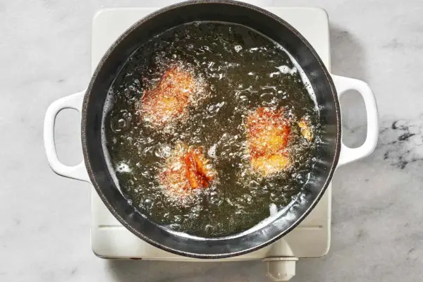 Três bolos de batata com gordura de pato fritando em óleo em um grande forno holandês