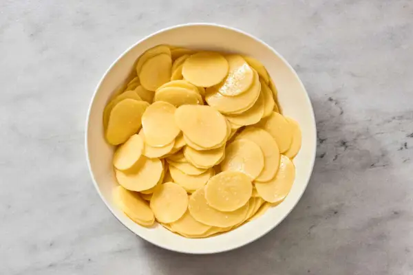 Uma tigela grande de batatas fatiadas misturadas com gordura de pato e sal