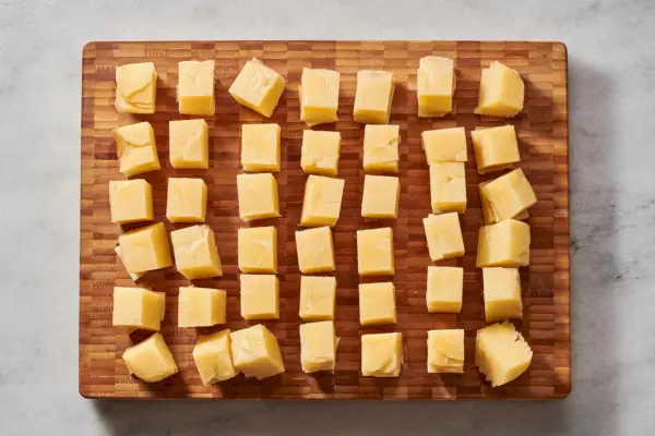 Uma tábua de corte com 42 cubos pequenos de bolos de batata com gordura de pato