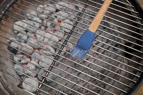 Eine Silikonbürste, die die Roste eines Holzkohlegrills ölt