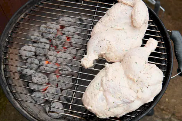 Ein Holzkohlegrill mit zwei in Joghurt marinierten Hähnchenhälften, die mit der Schnittfläche nach unten gegrillt werden