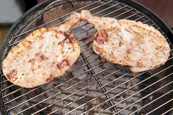 Ein Holzkohlegrill mit zwei mit Joghurt marinierten Hähnchenhälften, die über direkter Hitze gegrillt werden