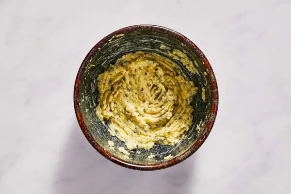 Un tazón pequeño de mantequilla mezclada con ajo, hierbas, ralladura de limón, sal y pimienta.