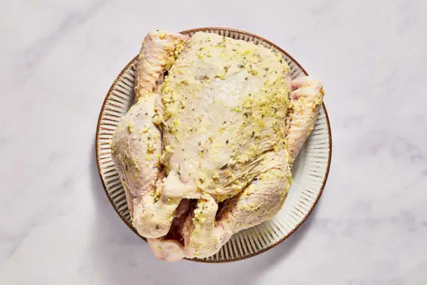Un pollo entero con mantequilla de hierbas debajo de la piel, untado encima de la piel y cubierto con sal y pimienta.