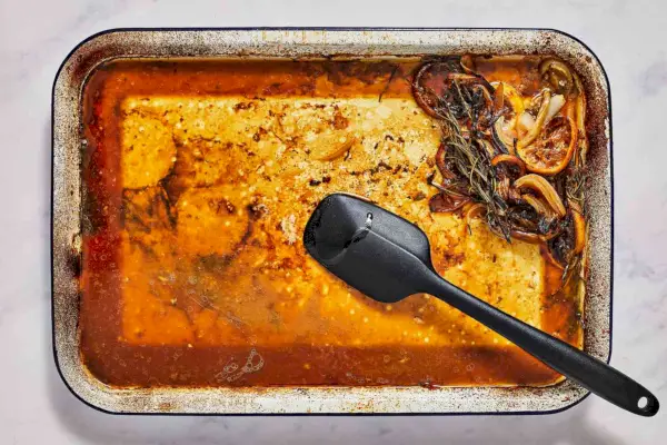 Una fuente para asar con jugos de pollo que se revuelve con una espátula de goma.