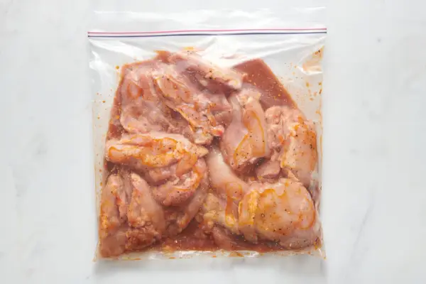 Una bolsa con cierre con muslos de pollo sin piel en una marinada de pepinillos en salmuera y cayena