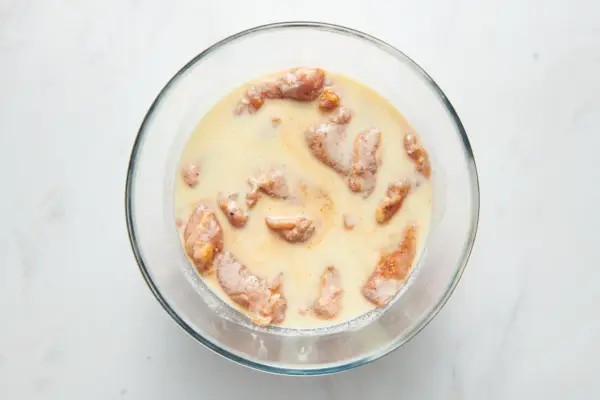 Un tazón grande de muslos de pollo marinados en una mezcla de suero de leche y huevo