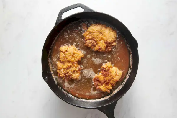 Una sartén grande con tres trozos de pollo fritos en aceite.