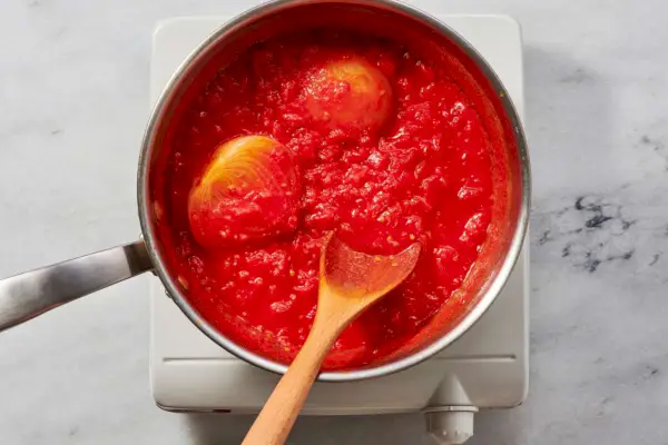 Una pentola di pomodori tritati, cipolla, burro e sale che bolle a fuoco lento, mescolando con un cucchiaio di legno