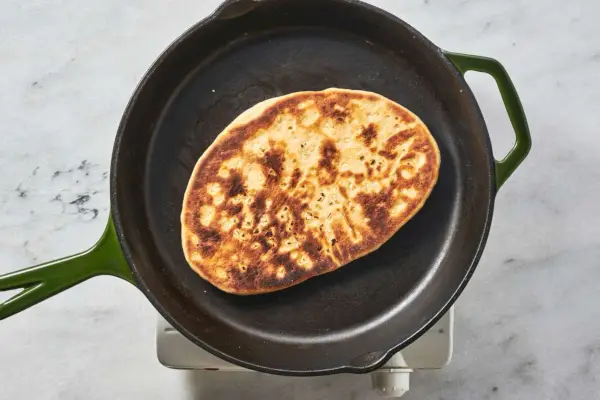 Un trozo de naan con ajo dorado en una sartén de hierro fundido