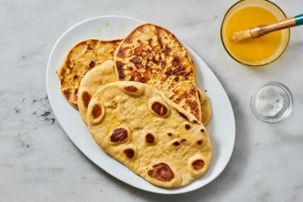 Un plato de pan naan con ajo con un plato de mantequilla derretida y una brocha de repostería