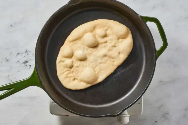 Un trozo de naan de ajo burbujeante en una sartén de hierro fundido