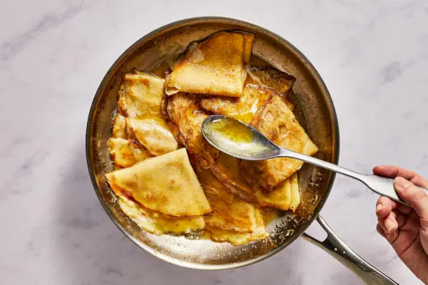 Eine große Pfanne mit Crêpes in Butter-Orangen-Sauce, begossen mit zusätzlicher Sauce