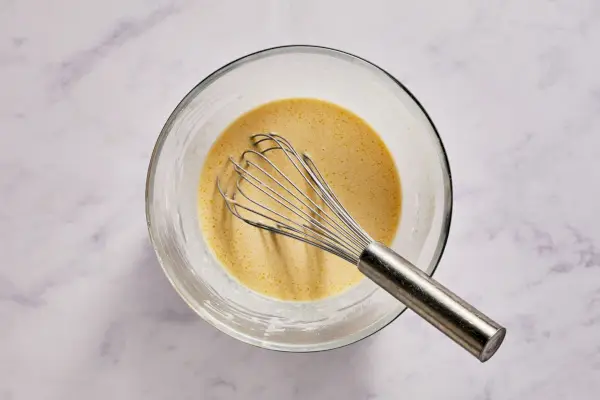 Eine große Schüssel mit Eiern, Mehl, Milch, Zucker, Wasser, Öl und geschmolzener Butter, die verrührt werden