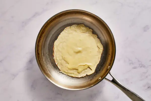 Eine große, geölte Pfanne, in der ein Crêpe zubereitet wird