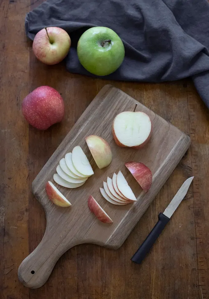 czerwone jabłka pokrojone na kawałki dla fanów jabłek na desce do krojenia otoczonej jabłkami i nożem' title=