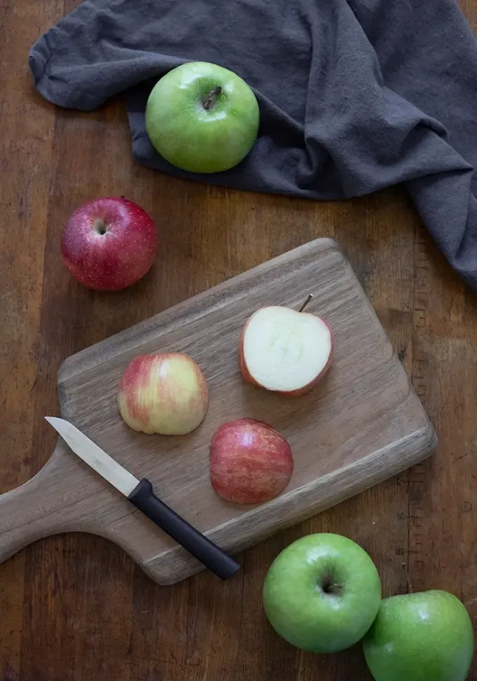 deska do krojenia z jabłkami pokazująca dwa sposoby ułożenia połówek jabłka przed pocięciem plasterków jabłka' title=