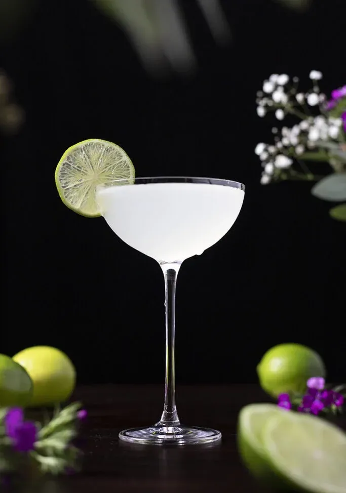 un cocktail freddo e ghiacciato in un bicchiere da coupé con una ruota di lime.' title=