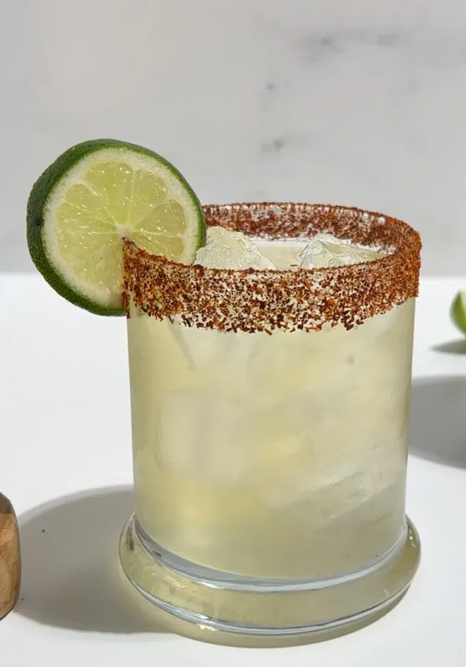 margarita servita con ghiaccio con bordo guarnito con Tajin rossastro.' title=