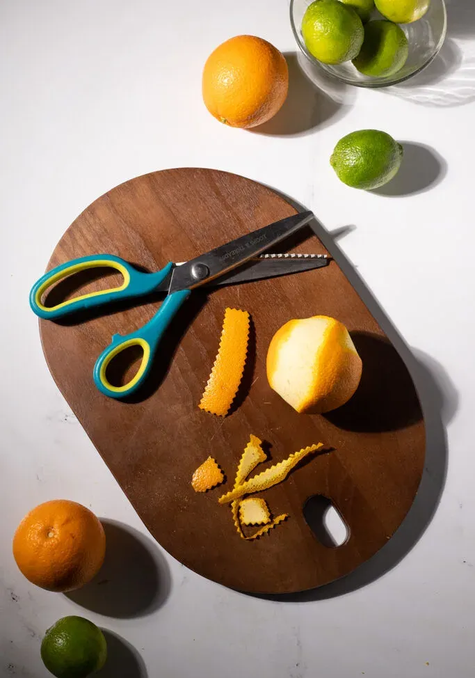 una cáscara de naranja cortada en un rectángulo con bordes puntiagudos junto a unas tijeras dentadas.' title=