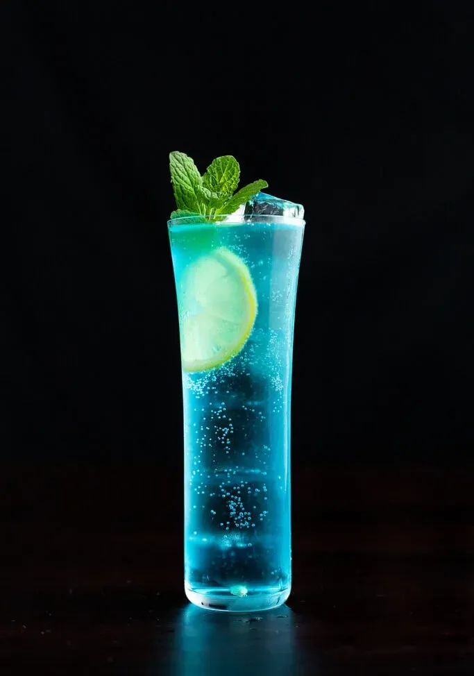 Cóctel azul en un vaso alto adornado con menta.' title=