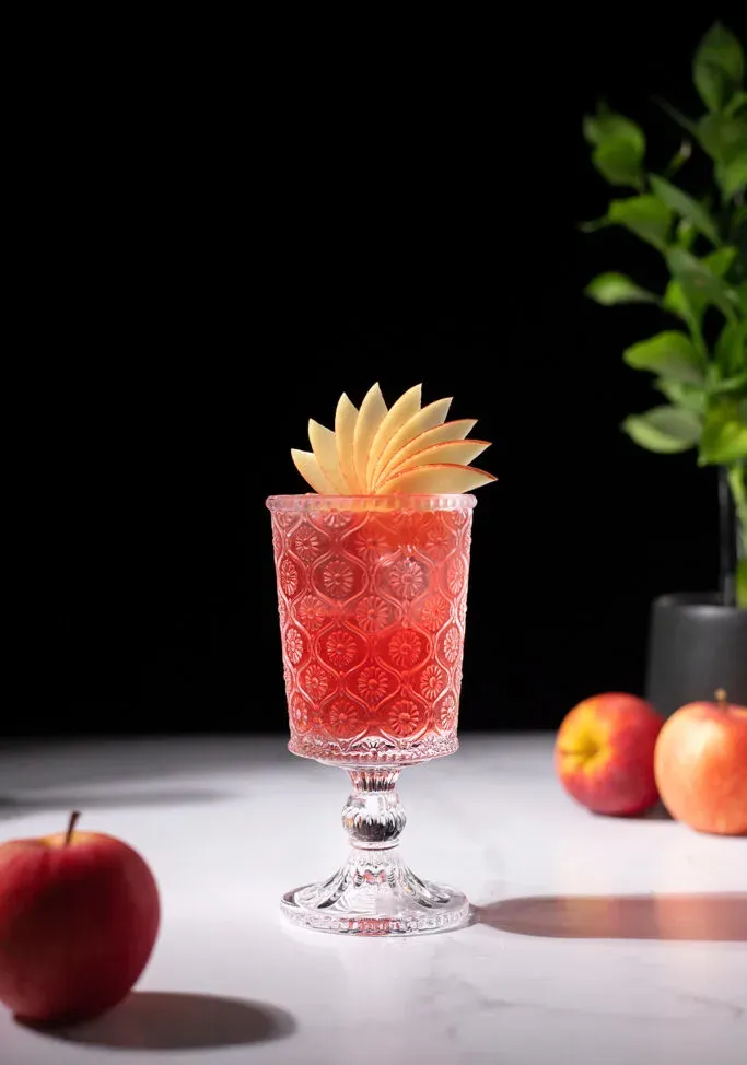 una bebida roja adornada con un elegante abanico de manzana.' title=