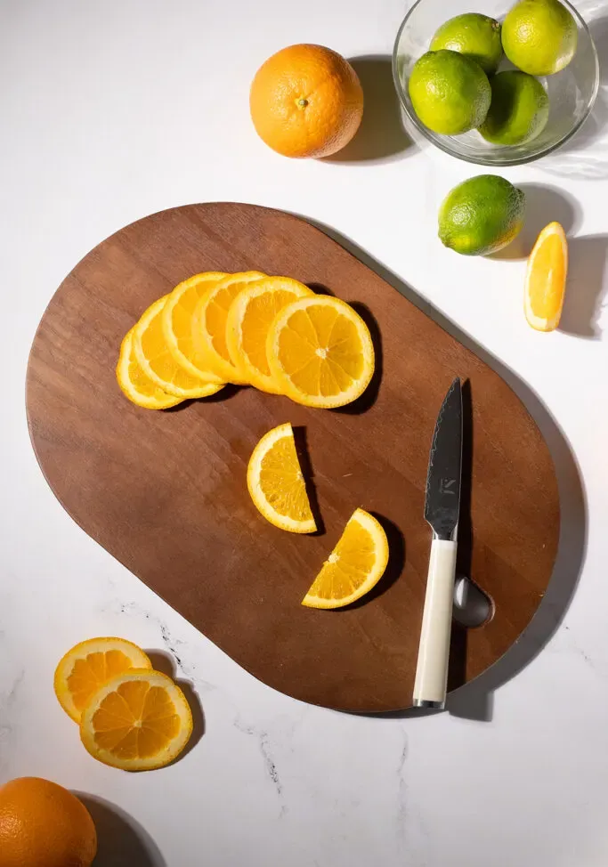 varias ruedas de naranja y dos rodajas de naranja sobre una tabla de cortar.' title=