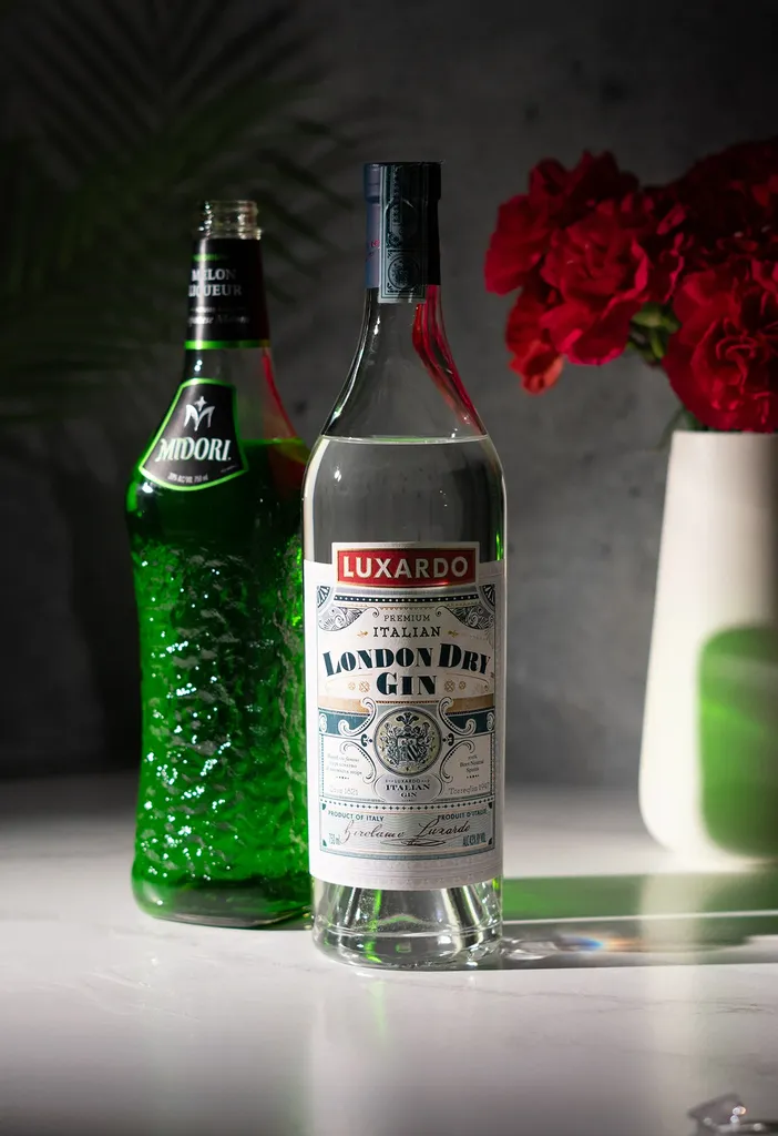 bottiglia di Luxardo London Dry Gin accanto alla bottiglia di liquore verde al melone Midori.' loading='lazy' title=