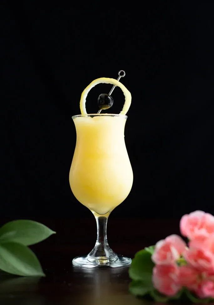 coquetel amarelo congelado decorado com um círculo de casca de limão e cereja.' loading='lazy' title=
