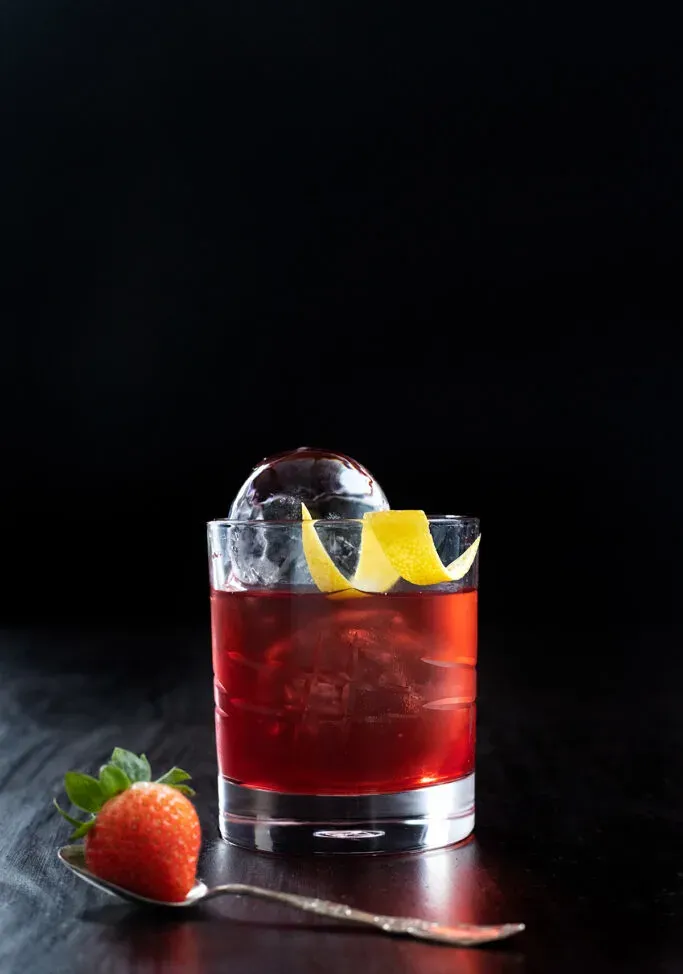 ein rotes Getränk mit klaren Eiskugeln in einem Steinglas.' loading='lazy' title=