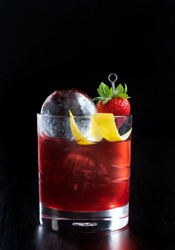 ein rotes Getränk mit einer Erdbeere auf einem Cocktailspieß.' title=