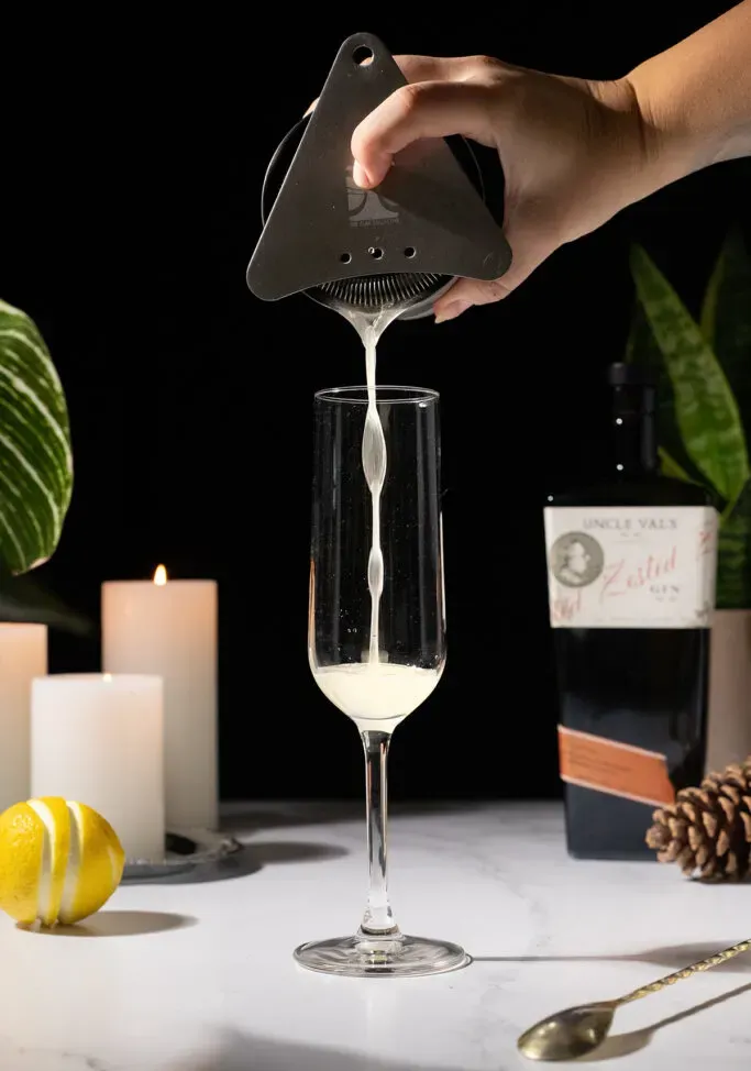 Den Cocktail aus einem Shaker in eine Champagnerflöte abseihen.' loading='lazy' title=