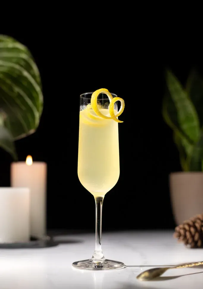 ein gelber, sprudelnder Cocktail in einer Champagnerflöte mit einer langen Zitronennote.' title=