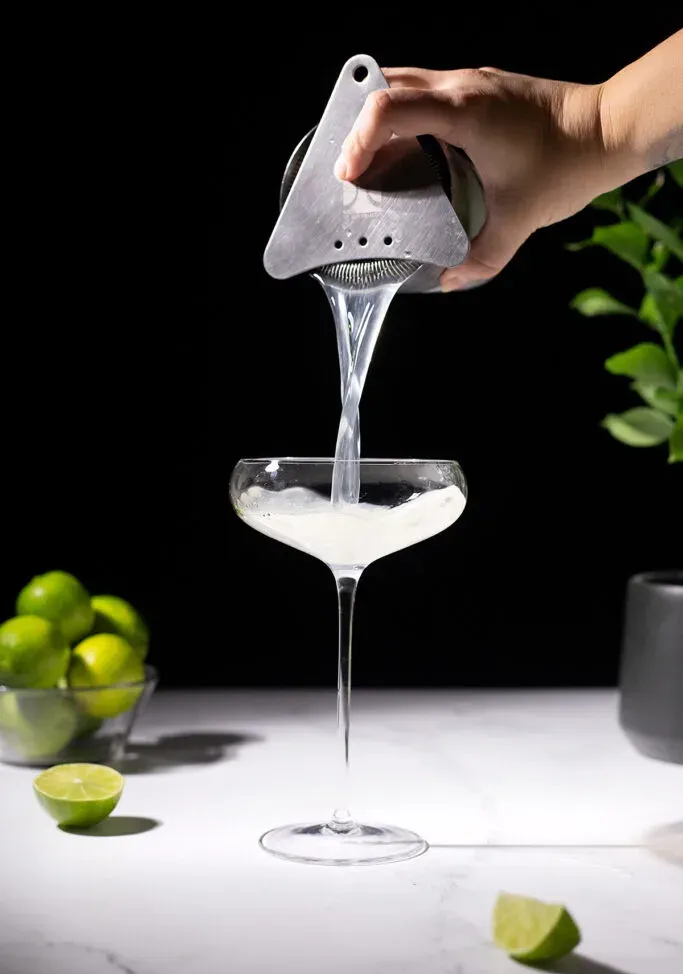 verser un cocktail clair dans un grand verre coupé.' title=