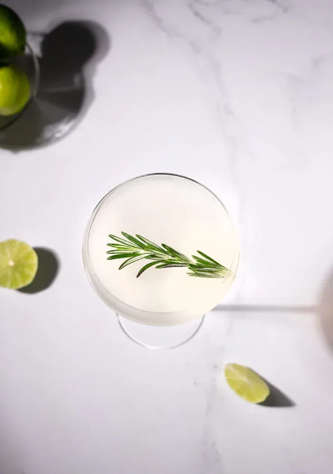 gros plan d'une boisson trouble dans un verre coupé garni d'un brin de romarin.' title=
