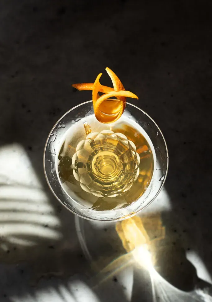 una vista aérea de un martini amarillo pálido en un vaso grabado vintage.' title=