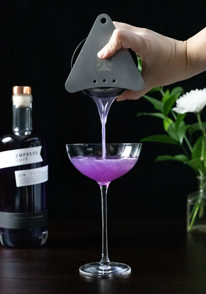 Einen violetten Cocktail in ein Coupéglas abseihen' loading='lazy' title=