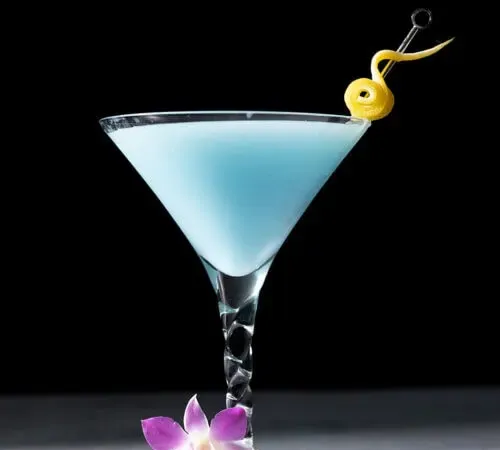 黒い背景にレモンをひねったマティーニグラスに入ったスカイブルーの飲み物。' title=