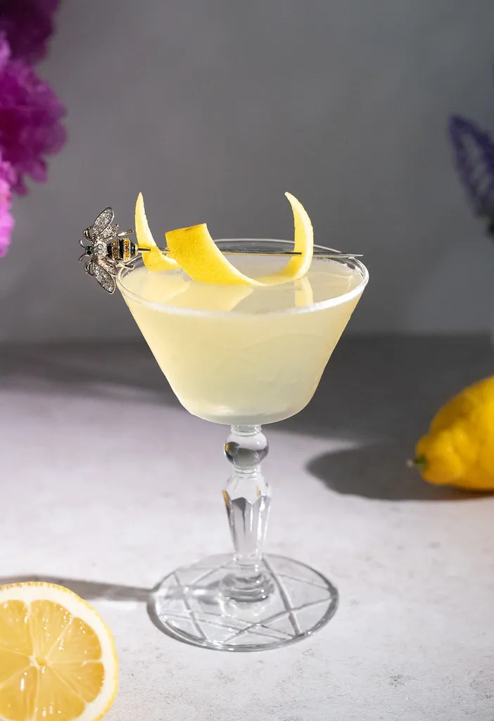 žltý koktail s oblohou z citrónovej kôry vedľa citrónov.' title=