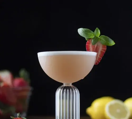 cocktail rose dans un verre coupé garni d'une fraise.' title=