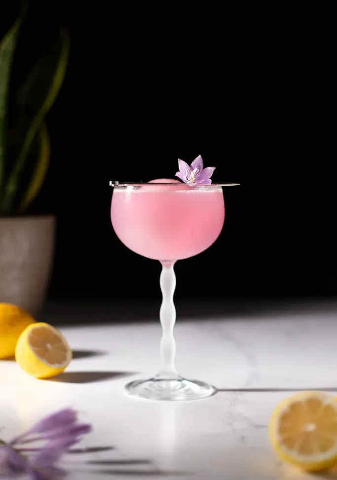 משקה ורוד בכוס קופה עם פרח סגול.' title=