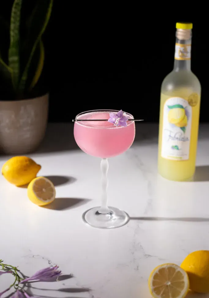 קוקטייל ורוד לצד לימונים ובקבוק לימונצ'לו.' title=