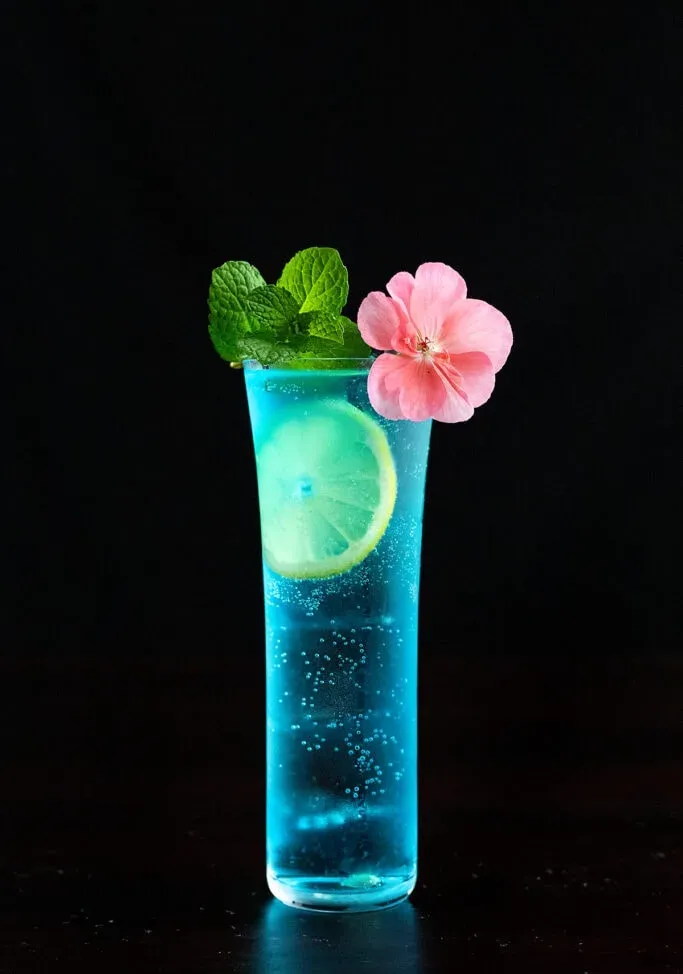 レモン ホイール ミントの小枝とピンクの花が入った青い AMF カクテル。' title=