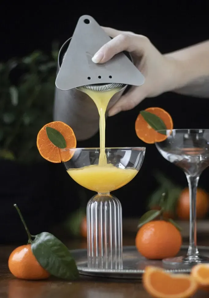 versando un gin sour al mandarino in un bicchiere da coupé da uno shaker.' loading='lazy' title=