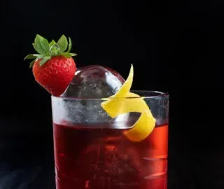 uma bebida vermelha brilhante em um copo baixo com um toque de morango e limão.' title=