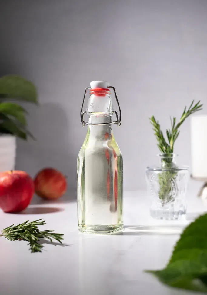 eine Bügelverschlussflasche voller hellgrünem Sirup neben Rosmarin und Äpfeln.' loading='lazy' title=