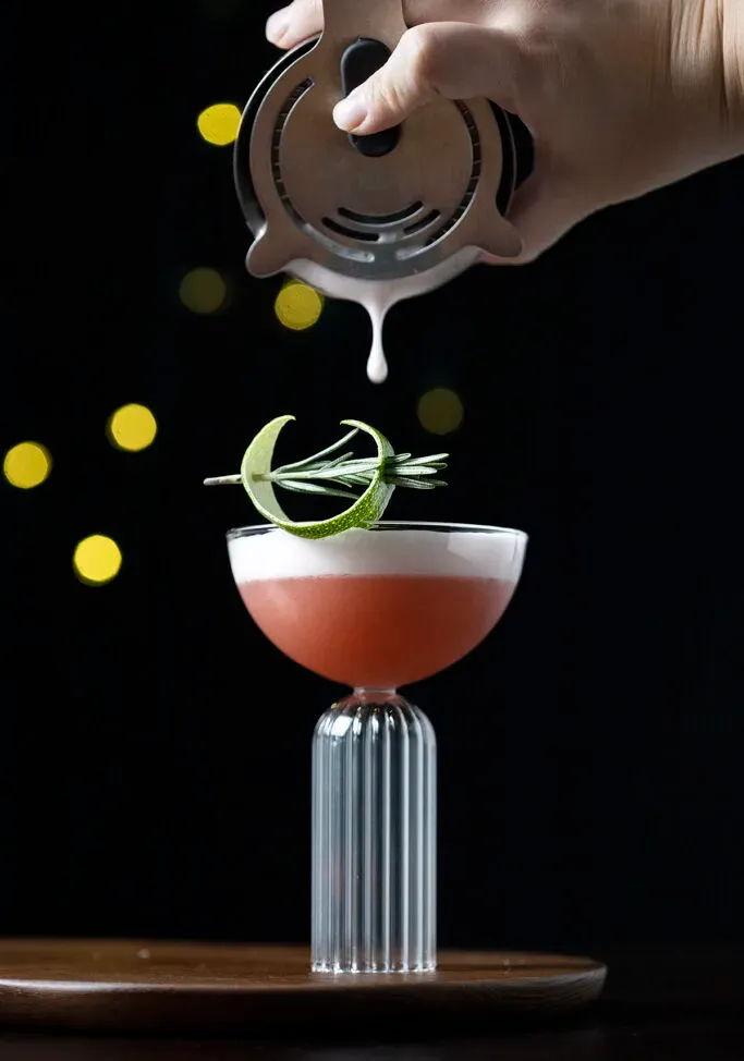 Ein Tropfen weißer Schaum, der aus einem Cocktailshaker in ein Getränk fällt.' title=